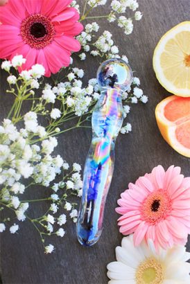 Photo du dildo en verre Icicles n°08 de la marque Pipedream, au soleil sur une table accompagné de jolies fleurs.