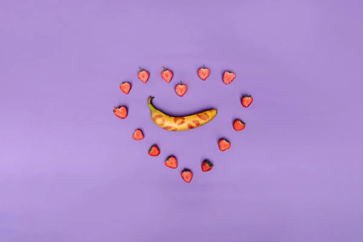 une banane avec des marques de rouge à lèvres entourées par des fraises en coeur