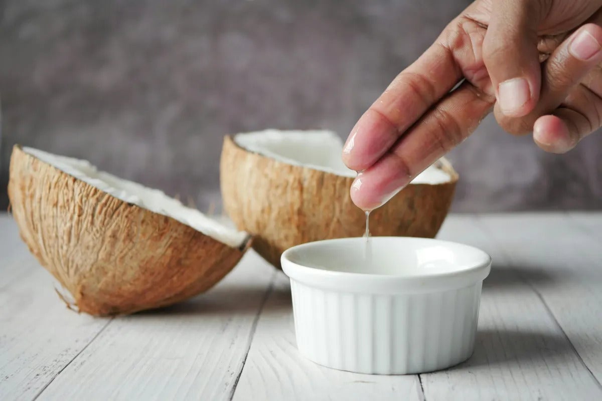 deux doigts ont trempés dans un recipient et on voit des noix de coco en arrière plan