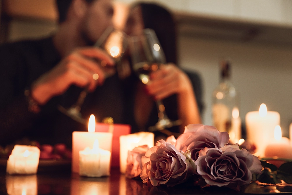 Couple partageant un moment romantique avec roses et bougies, autour d’une coupe de vin.