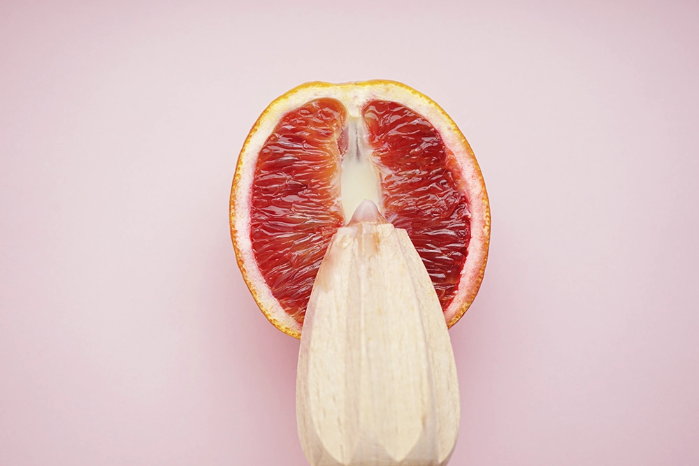 Moitié d’orange sanguine sur fond rose avec un presse-agrume pour symboliser un sextoy trop gros.