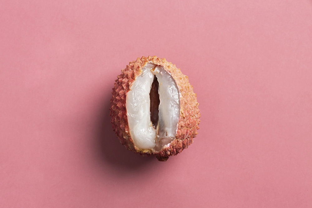 Litchi ouvert sur fond rose, symbolisant le titre “Quel premier sextoy choisir, selon ses envies et besoins ?”.