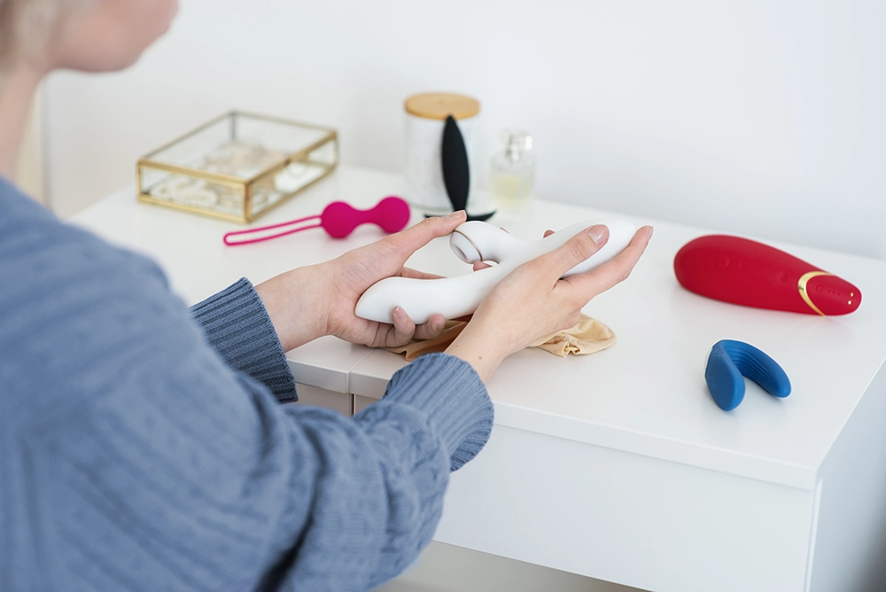 Jeune femme comparant différents modèles de sextoys posés sur une table de chevet.